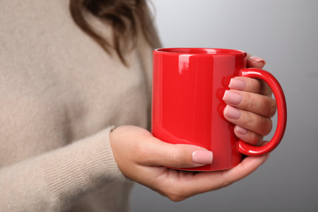 Woman holding red mug on light gray background, closeup. Mockup for designの写真素材