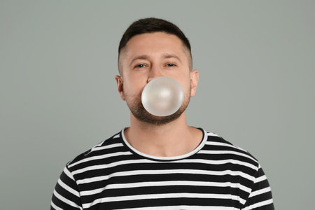 Handsome man blowing bubble gum on light grey backgroundの写真素材
