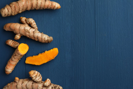 Whole and cut turmeric roots on blue wooden table, flat lay. Space for textの写真素材
