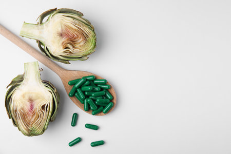 Spoon with pills and fresh artichoke on white background, flat lay. Space for textの写真素材