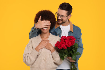 International dating. Handsome man presenting roses to his beloved woman on orange backgroundの写真素材