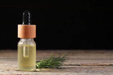 Bottle of essential oil and fresh dill on wooden table against black background, space for textの写真素材