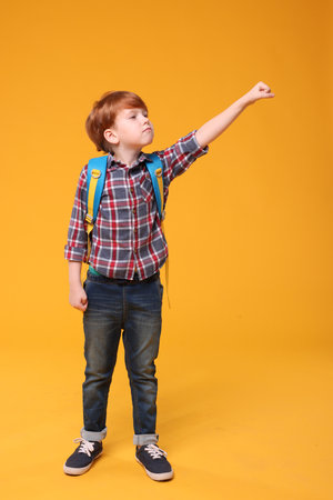 Cute schoolboy with backpack on orange backgroundの写真素材
