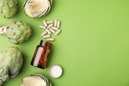 Bottle with pills and fresh artichokes on light green background, flat lay. Space for textの写真素材