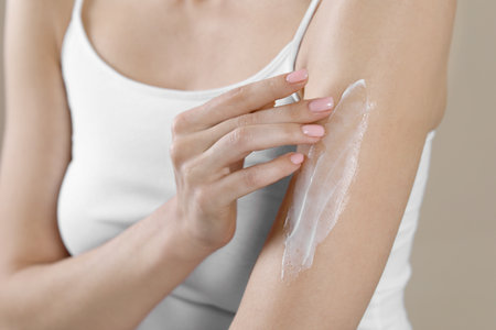 Woman applying body cream onto arm on beige background, closeupの写真素材