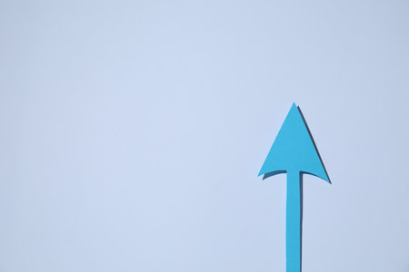 Light blue paper arrow on white background, top view. Space for text