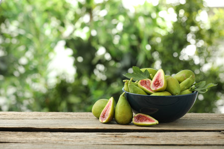 Cut and whole green figs on wooden table against blurred background, space for textの写真素材