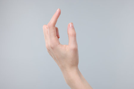 Woman holding something in fingers on gray background, closeupの写真素材