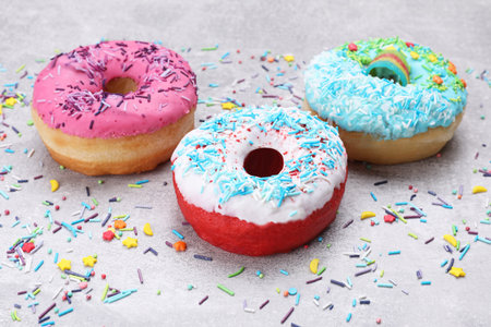 Sweet glazed donuts decorated with sprinkles on light gray table. Tasty confectioneryの写真素材