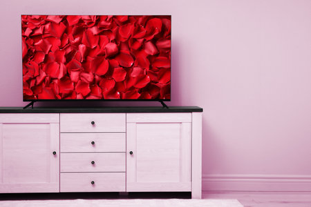 TV screen with red rose petals on commode near pink wall in room, space for textの写真素材
