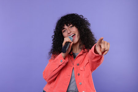 Beautiful young woman with microphone singing on purple backgroundの写真素材