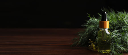 Bottle of dill essential oil on wooden table against black background. Banner design with space for textの写真素材