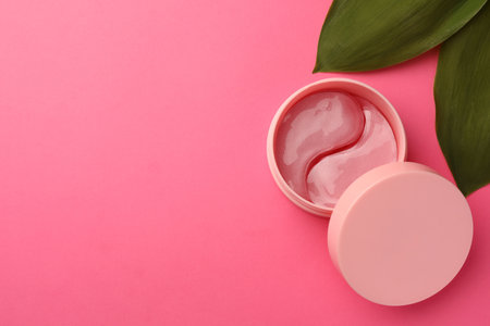 Jar of under eye patches and green leaves on pink background, flat lay with space for text. Cosmetic productの写真素材