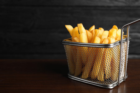 Frying basket with tasty French fries on wooden table, closeup. Space for text