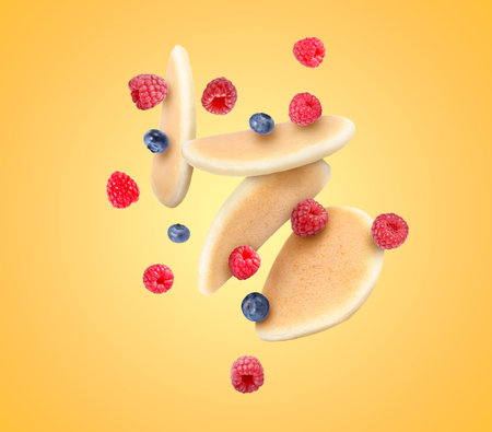 Many fresh pancakes and berries flying on golden backgroundの写真素材