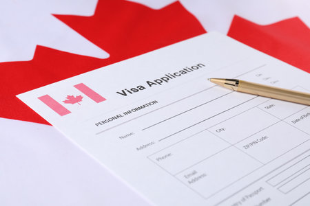 Immigration to Canada. Visa application form and pen on flag, closeupの写真素材