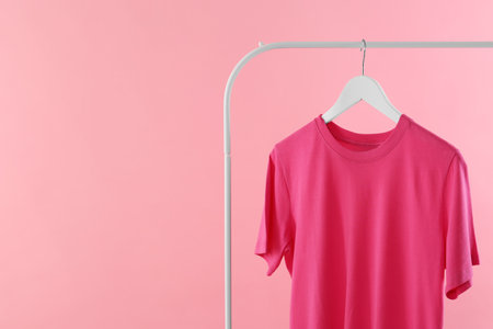 Rack with stylish t-shirt on pink background. Space for textの写真素材