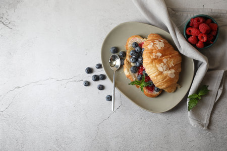 Delicious croissant with berries, almond flakes and spoon on light gray table, flat lay. Space for textの写真素材