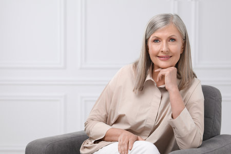 Portrait of beautiful senior woman in armchair indoors. Space for textの写真素材