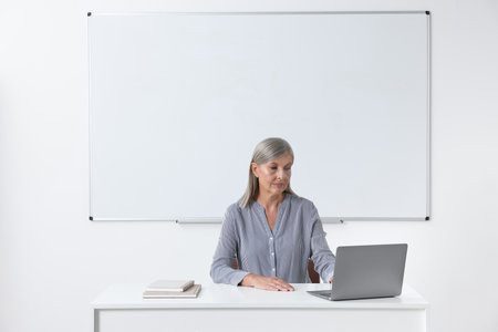 Professor sitting near laptop at desk in classroomの写真素材