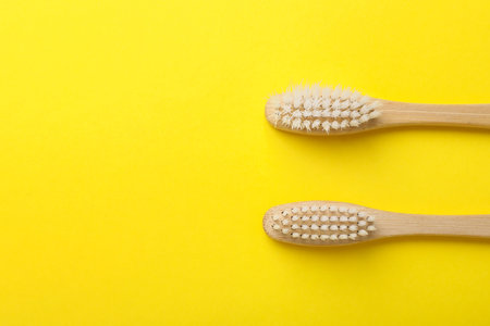 Bamboo toothbrushes on yellow background, flat lay. Space for text