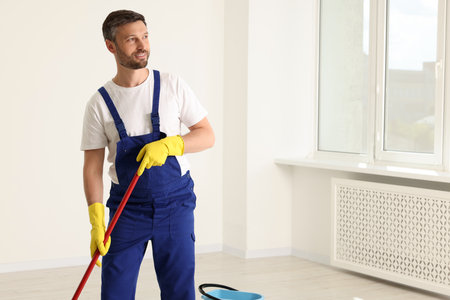Man in uniform cleaning floor with mop indoors. Space for textの写真素材