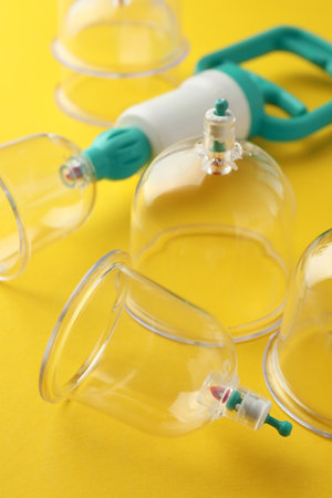 Plastic cups and hand pump on yellow background, closeup. Cupping therapyの写真素材
