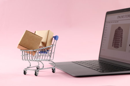 Online store. Laptop, mini shopping cart and parcels on pink backgroundの写真素材