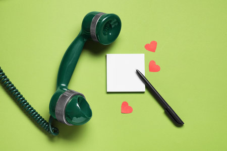 Long-distance relationship concept. Telephone receiver, empty note, paper hearts and pen on light green background, flat lay. Space for textの写真素材