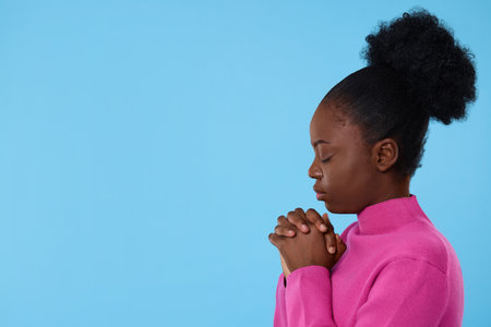 Woman with clasped hands praying to God on light blue background. Space for textの写真素材