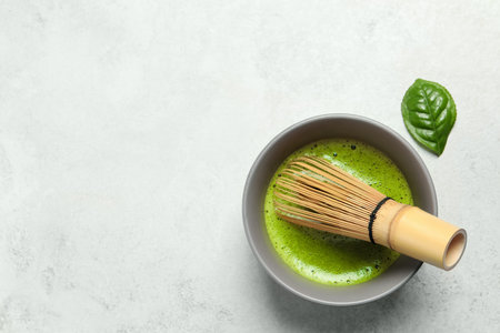 Cup of fresh green matcha tea with bamboo whiskey on light gray table, top view. Space for textの写真素材