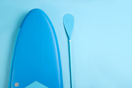 Board and paddle for standup paddleboarding (SUP) on light blue background, flat lay. Space for textの写真素材