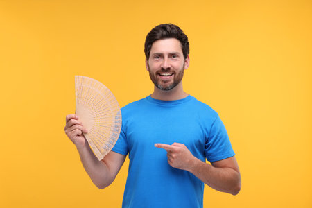 Happy man holding hand fan on orange backgroundの写真素材