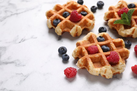 Delicious Belgian waffles with fresh berries and mint on white marble table, closeup. Space for text