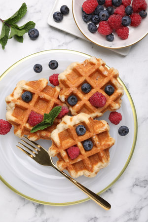 Delicious Belgian waffles with fresh berries and mint on white marble table, flat lay
