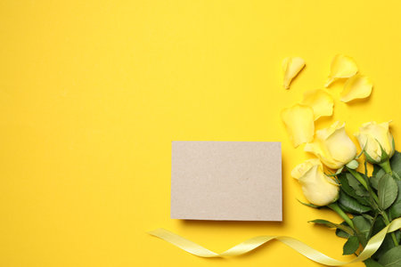 Beautiful roses, petals and blank card on yellow background, flat lay. Space for textの写真素材