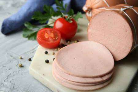 Delicious boiled sausage with tomatoes, parsley and spices on gray textured table, closeup