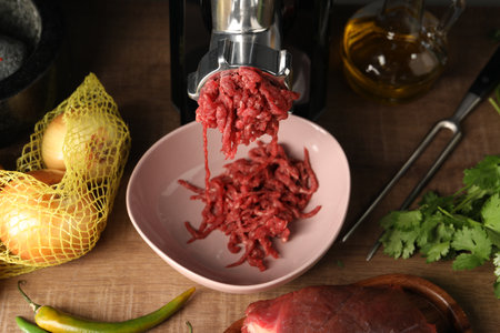 Mining beef with electric meat grinder on wooden table, above view