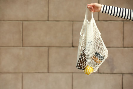 Conscious consumption. Woman with net bag of eco friendly products near stone wall, closeup. Space...