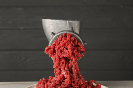 Metal meat grinder with beef mince against gray background
