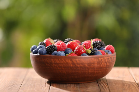 Bowl with different fresh ripe berries on wooden table outdoorsの写真素材