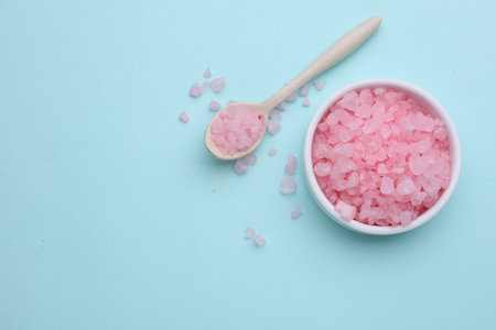 Bowl and spoon with pink sea salt on light blue background, flat lay. Space for textの写真素材