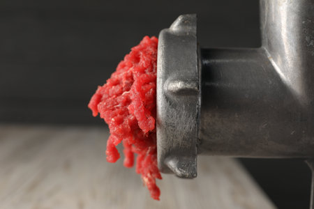 Mining beef with metal meat grinder on blurred background, closeup