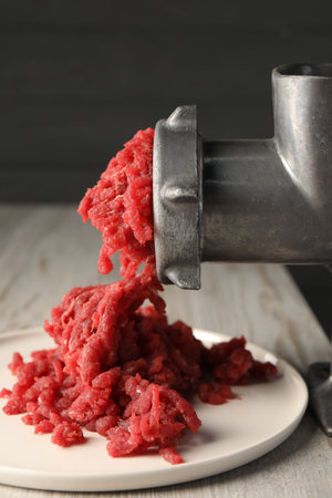 Mining beef with metal meat grinder on light wooden table, closeupの写真素材