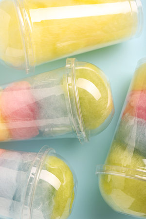Colorful cotton candies in plastic cups on light blue background, flat lay