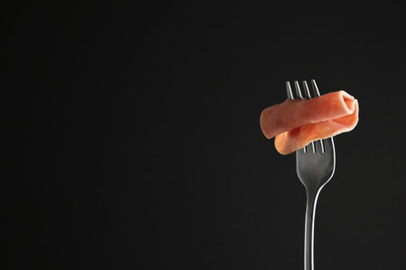 Fork with tasty slice of ham on black background, space for textの写真素材
