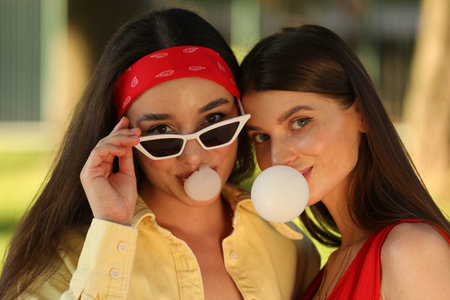 Beautiful young women blowing bubble gums outdoorsの写真素材