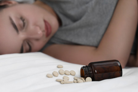 Depressed woman sleeping on bed near overturned bottle with antidepressants, selective focusの写真素材