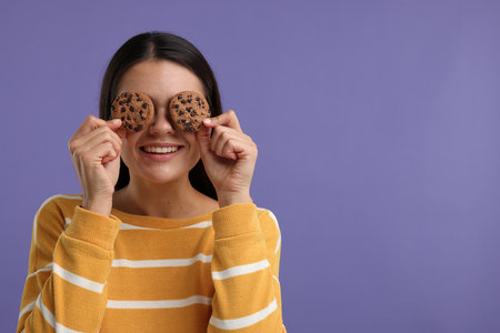 Young woman with chocolate chip cookies on purple background, space for textの写真素材