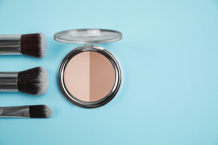 Face powder and brushes on light blue background, flat lay. Space for textの写真素材